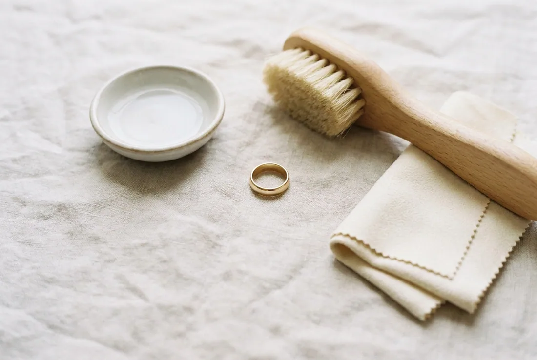 A soft brush, a dish of water and a polishing cloth beside a ring