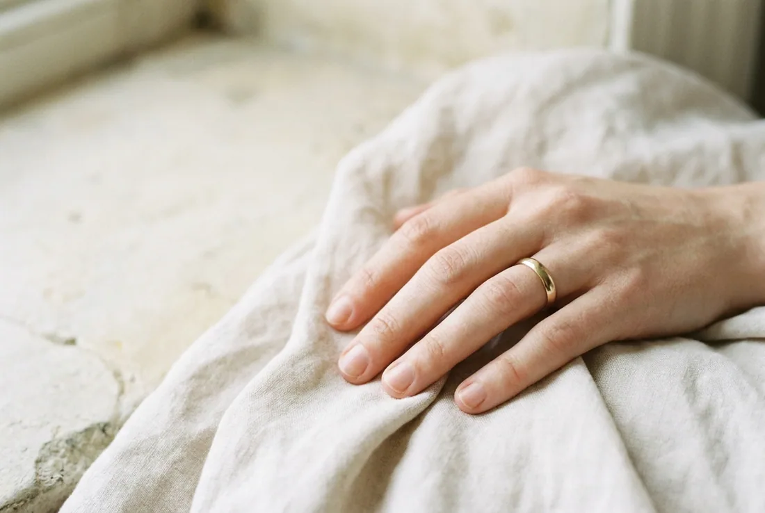 A left hand wearing a plain wedding band on the fourth finger