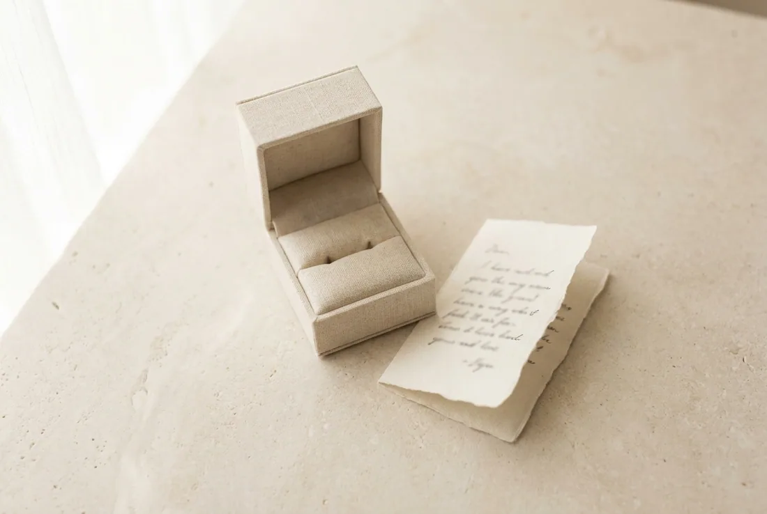 A handwritten note and an empty linen ring box on pale stone