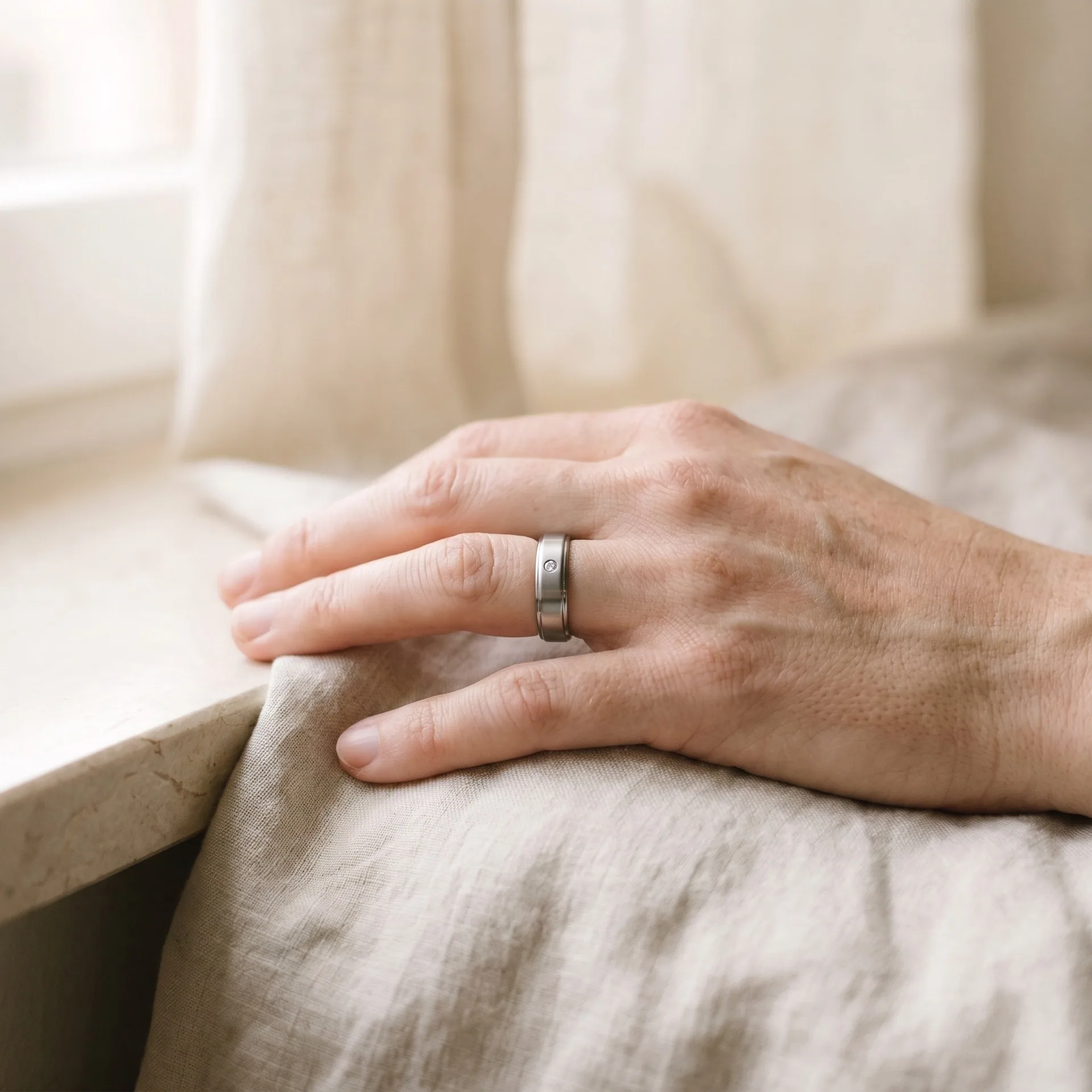 A single hand resting on linen, wearing one slim ring
