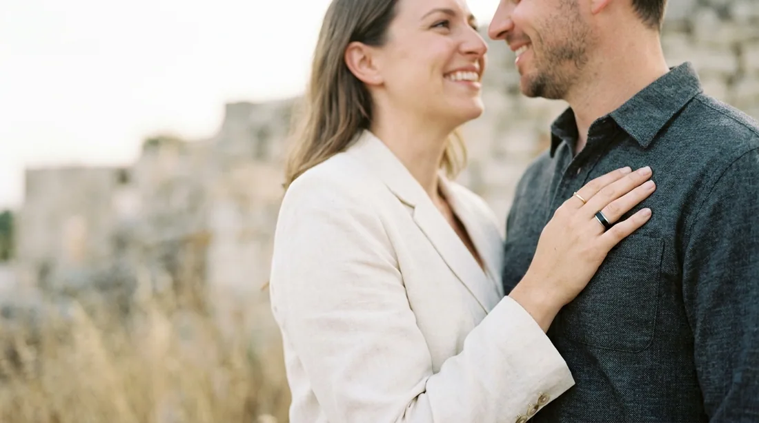 A married couple outdoors in evening light, both wedding bands visible
